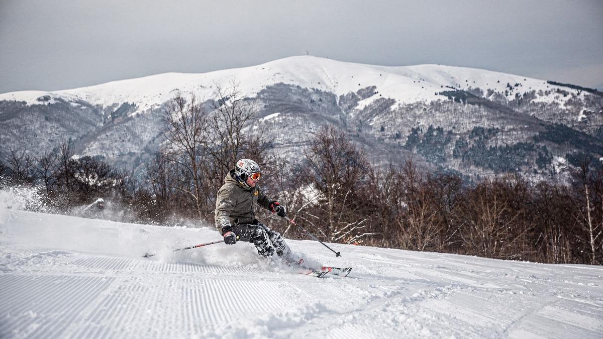 Skier descending a groomed piste above a snow-covered Carpathian valley at midday