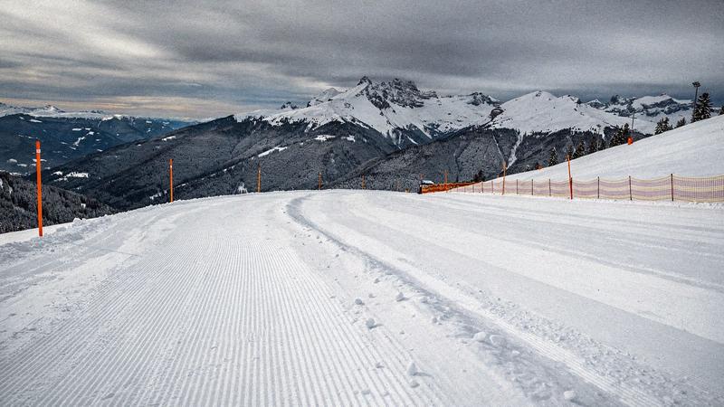 Groomed piste with safety poles below a ridgeline