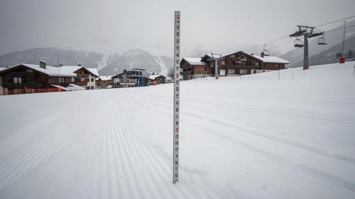 Snow depth stake on a groomed piste with resort buildings behind